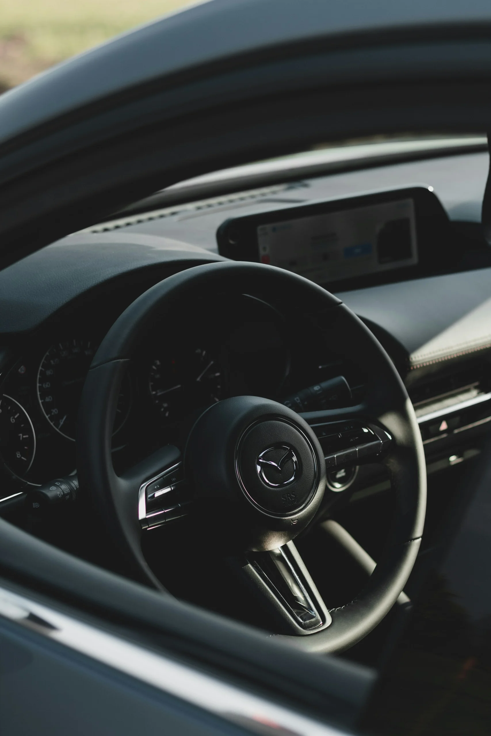 Mazda vehicle interior showing steering wheel, instrument cluster, and dashboard display