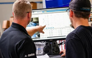 Technicians reviewing vehicle measurement data and repair analysis on computer screen