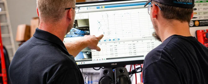 Technicians reviewing vehicle measurement data and repair analysis on computer screen